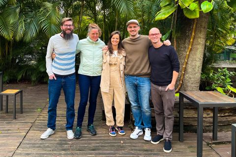 Five people stading on a wooden deck with foliage in the background